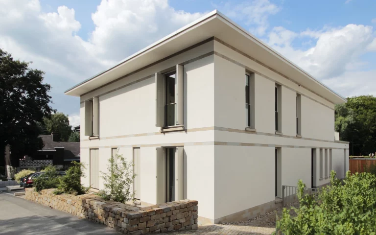 Neubau Haus D in Bochum Ansicht von der Straße mit Putzfassade mit Faltschiebeläden, eingelegten Bändern und Sockel sowie bepflanzter Bruchsteinmauer aus Ruhrsandstein.