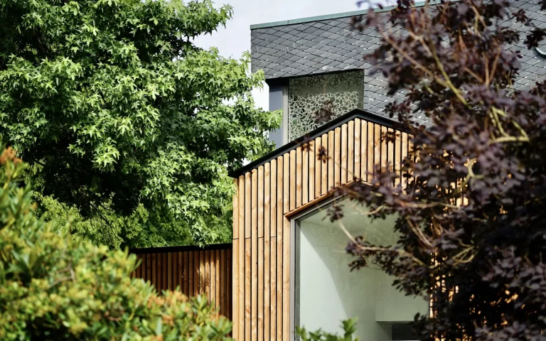 Umbau St. Altfrid in Essen Aussenansicht eines Details vom Eingang mit Oberlicht, Holzlattung, zurückliegendem Schieferdach, Kirchenkreuz, Attika und Oberlicht.