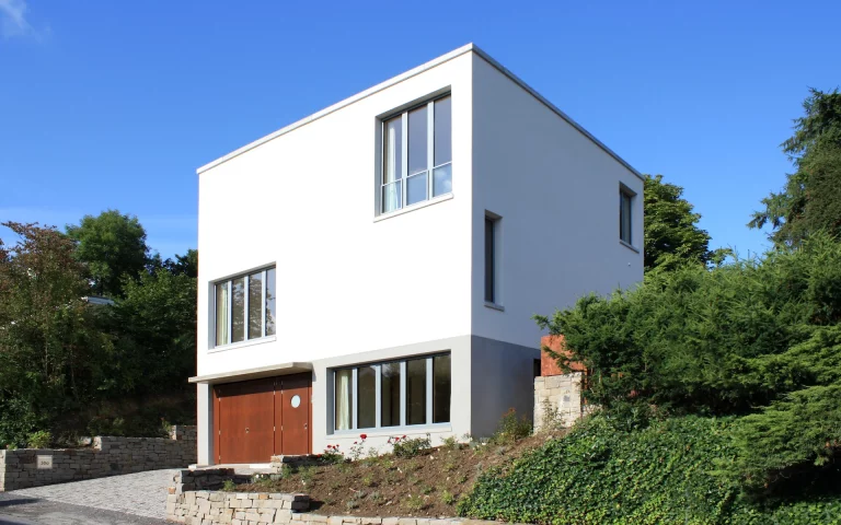Neubau Haus R in Velbert-Langenberg Ansicht von der Straße mit Putzfassade, Sichtbetonelementen sowie Pflaster und Bruchsteinmauern aus Ruhrsandstein.