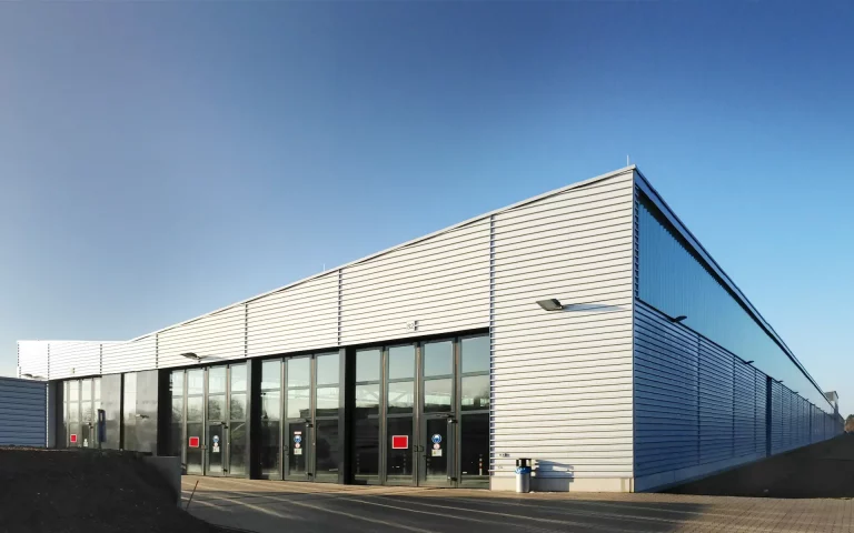 Erweiterung Siemens Zugbildungshalle 2 Ansicht Stirnseite mit Falttoren, Umfahrt, hinterlüfteter Trapezprofilblechfassade, Lichtband und Sichtbetonsockel.