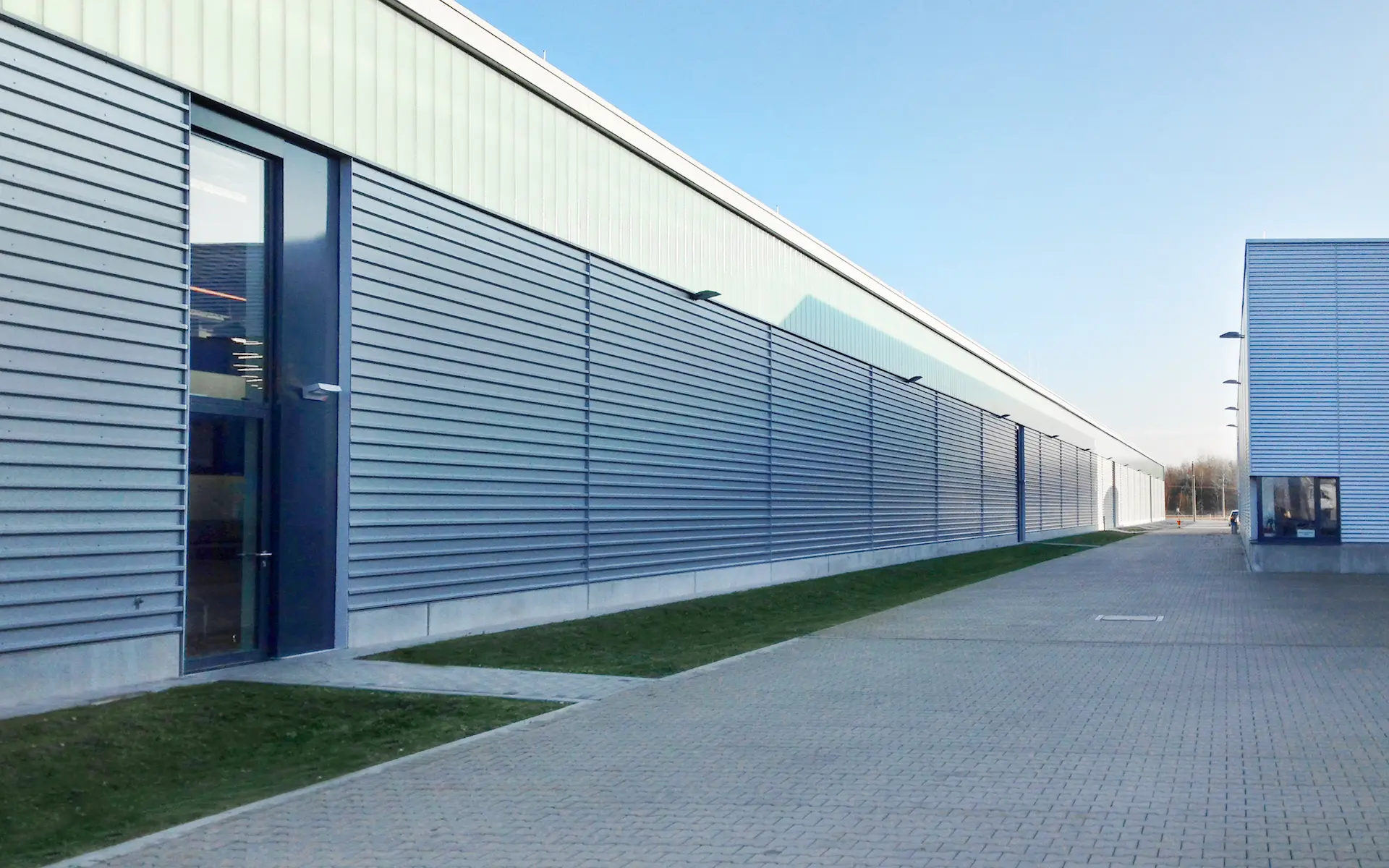 Erweiterung Siemens Zugbildungshalle 2 Ansicht Längsseite mit durchgehendem Lichtband, begrünten Rigolen, raumhohen verglasten Zugängen.
