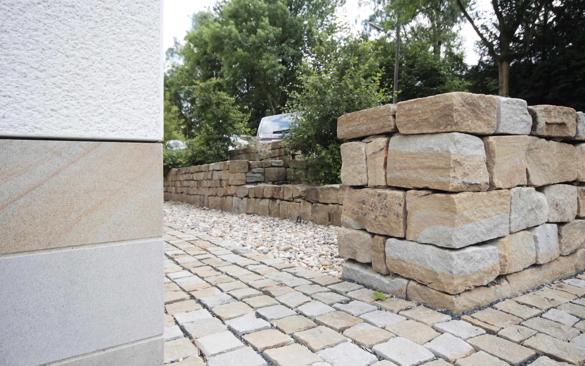 Neubau Haus D in Bochum Detail des Sockels, der bepflanzten Bruchsteinmauer sowie des Pflasters aus Ruhrsandstein mit unterschiedlichen Oberflächenbearbeitungen.
