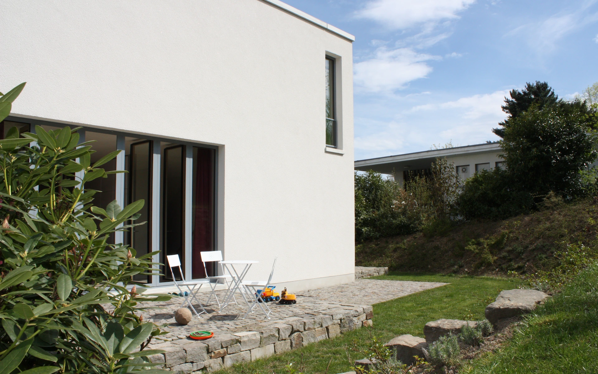 Neubau Haus R in Velbert-Langenberg Ansicht vom Garten mit Putzfassade, raumhohen Holz-Aluminium-Fenstern, Sichtbetonelementen sowie Pflaster, Bruchsteinmauern und Treppe aus Ruhrsandstein.