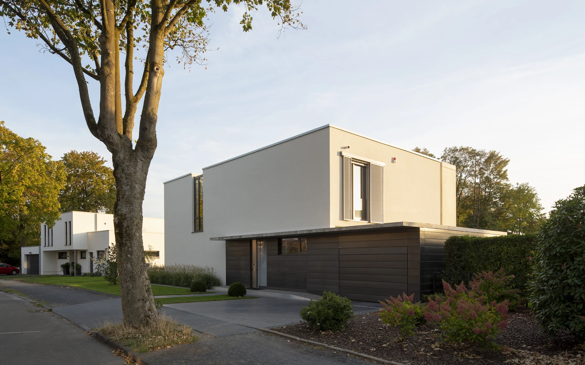 Neubau Haus K in Kamp-Lintfort Ansicht von der Straße am Nachmittag mit Eingang, Sichtbetonvordach, in die Dachfläche übergehendem Fenster und elektrischen Schiebeläden.