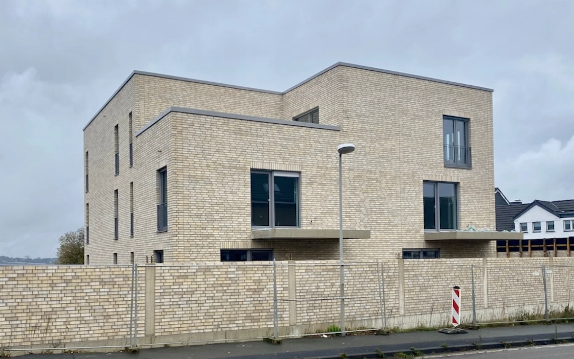 Neubau Mehrfamilienhaus in Ratingen Ansicht von der Landstraße im Bauzustand mit französischen Fenstern, Klinkerfassade aus Wasserstrichziegeln und Sichtbetonbalkonplatten.