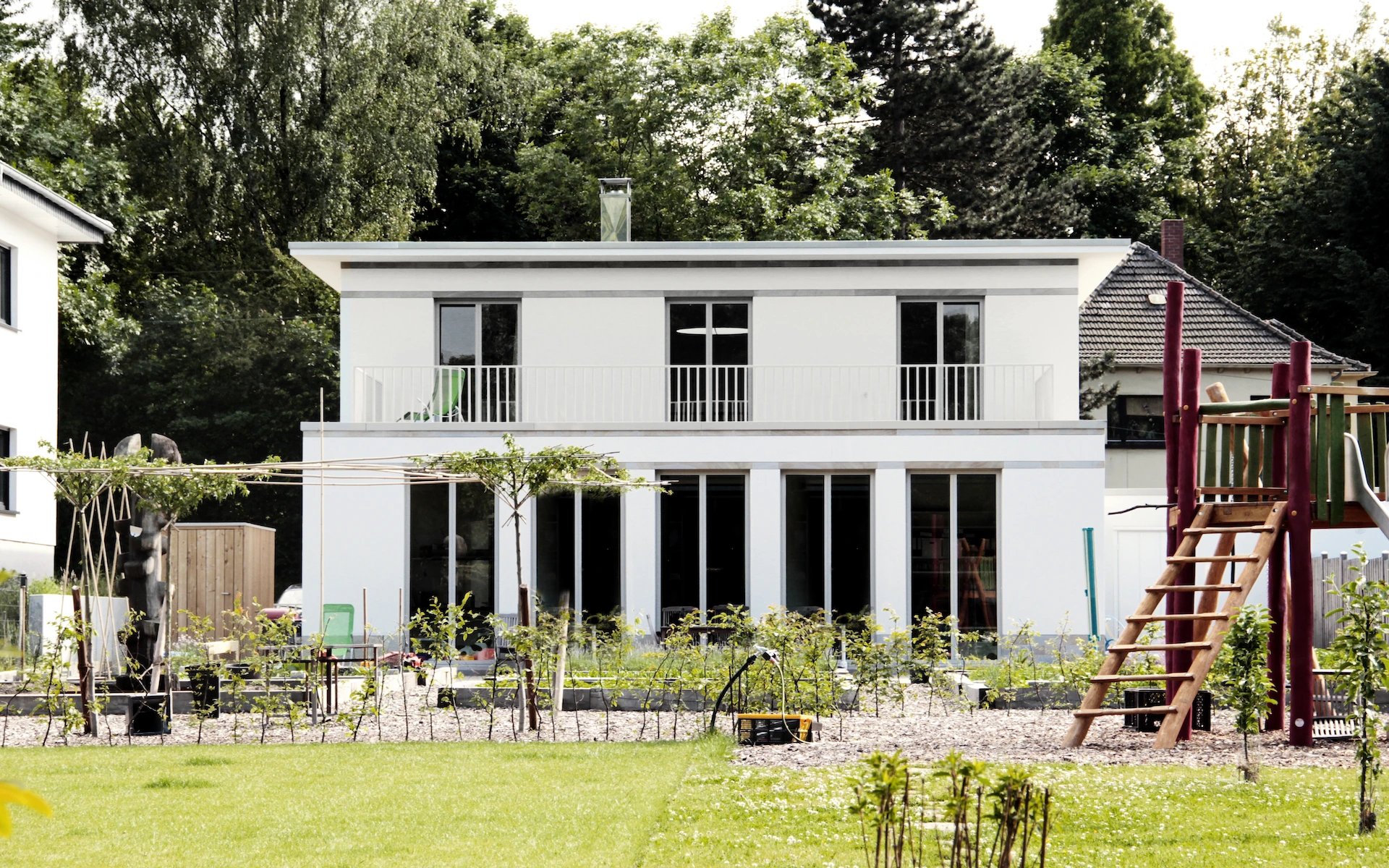 Neubau Haus D in Bochum Ansicht vom Garten mit Putzfassade mit französischen Fenstern, eingelegten Bändern und Sockel aus Ruhrsandstein.
