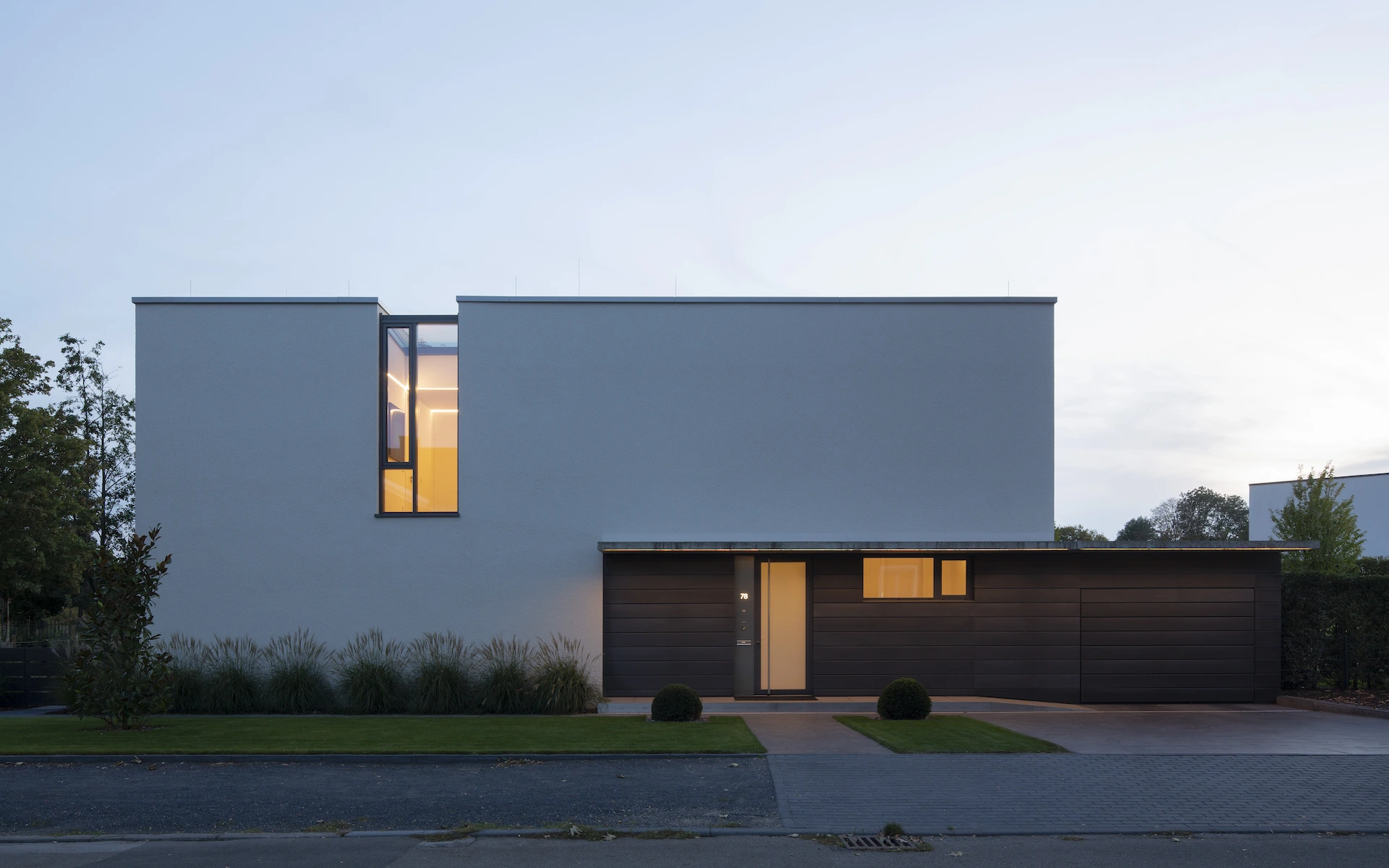 Neubau Haus K in Kamp-Lintfort frontale Ansicht von der Straße in der Dämmerung mit Eingang, Sichtbetonvordach und in die Dachfläche übergehendem Fenster.