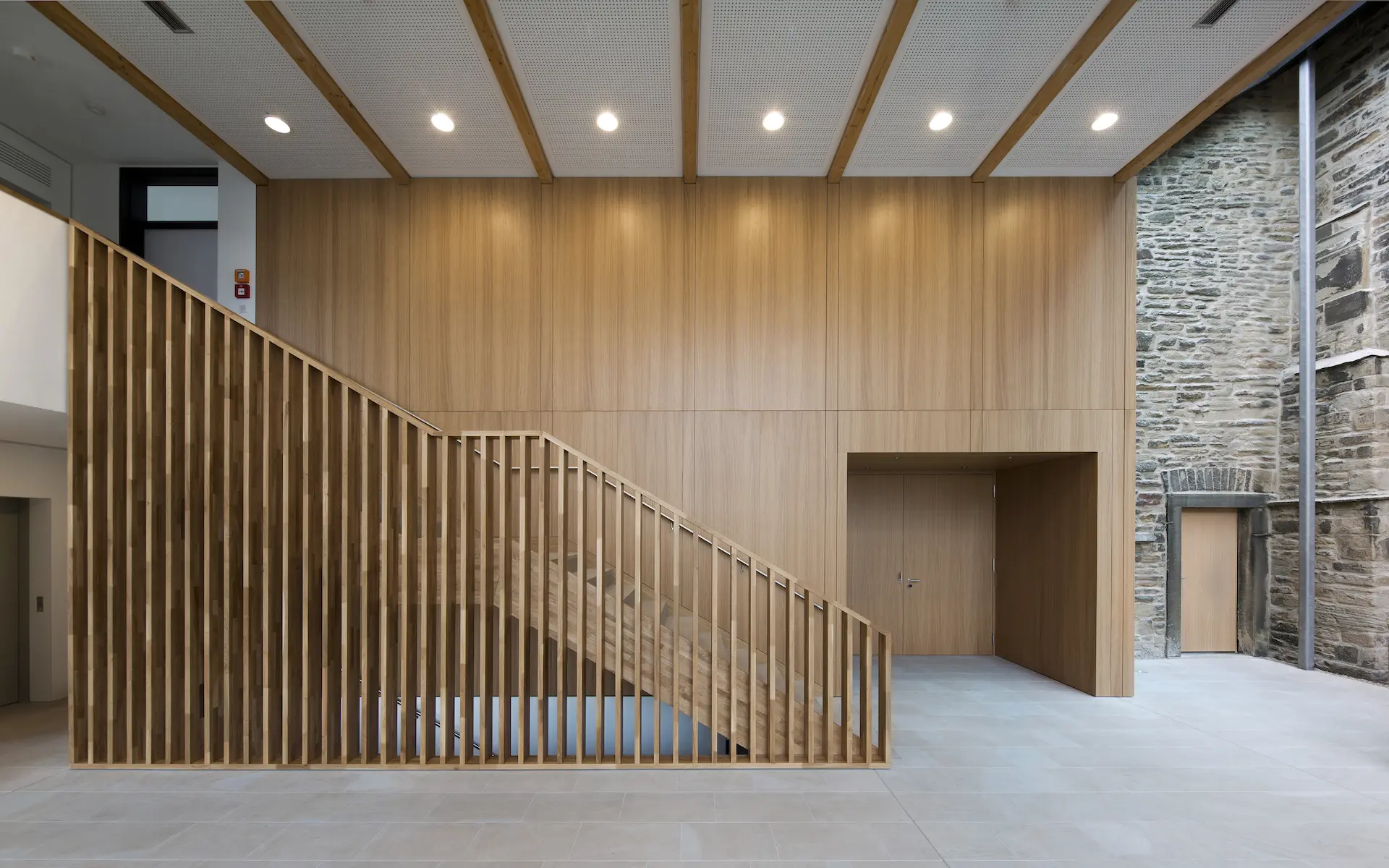 Neubau Gemeindezentrum St. Viktor Innenraum mit Blick ins Foyer mit Geländer als Holzharfe, Oberlicht, Galeriekante, Natursteinboden und Holzvertäfelung.
