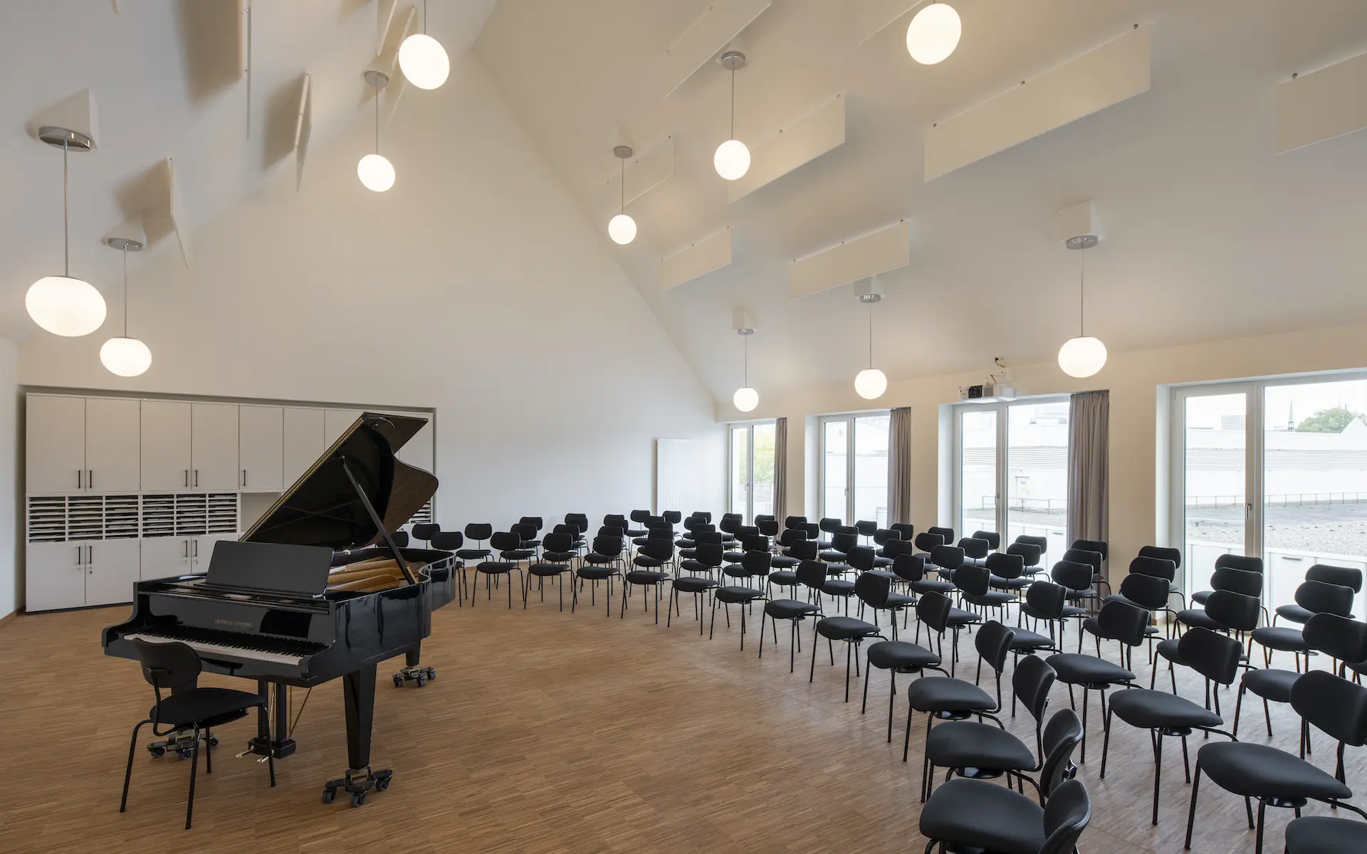 Umbau Haus der Kirchenmusik Essen Innenraum mit Blick in den großen Singsaal im neuen Dachgeschoss ist bestuhl mit 120 Sitzplätzen für Chöre, Flügel, Deckenleuchten, Stäbchenparkett.