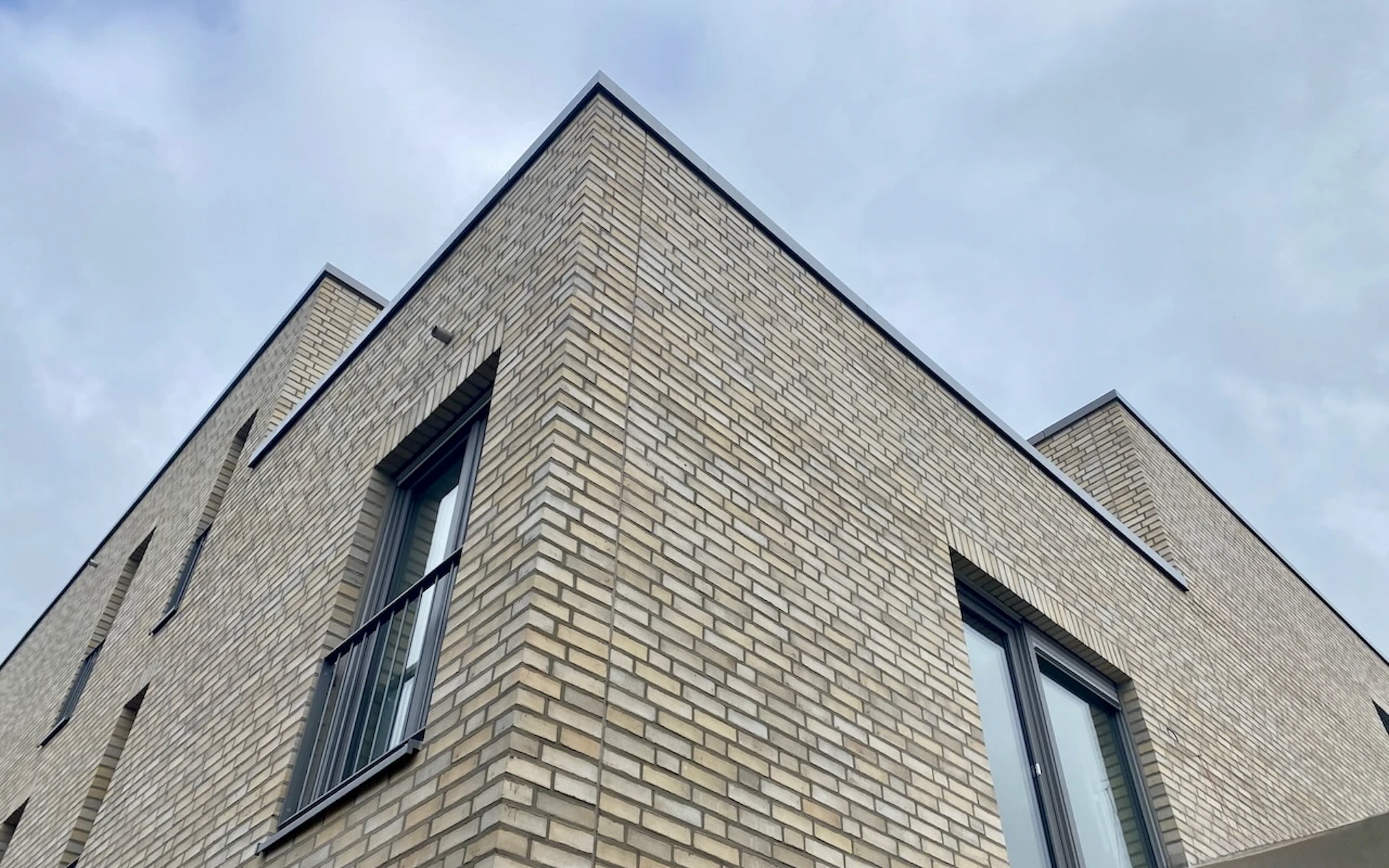 Neubau Mehrfamilienhaus in Ratingen Detail einer Gebäudeecke im Bauzustand mit französischen Fenstern und Klinkerfassade aus Wasserstrichziegeln.