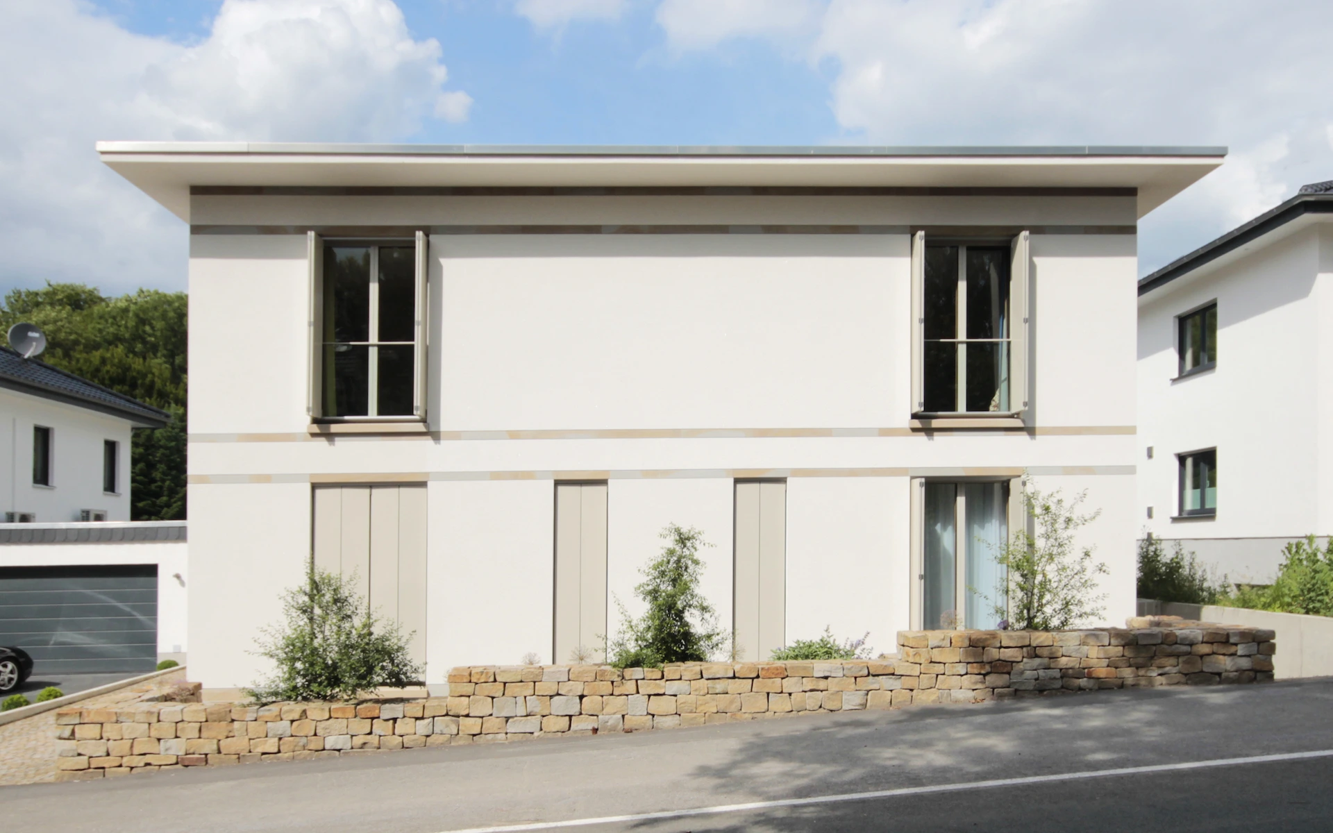 Neubau Haus D in Bochum frontale Ansicht von der Straße mit Putzfassade mit Faltschiebeläden, eingelegten Bändern und Sockel sowie bepflanzter Bruchsteinmauer aus Ruhrsandstein.