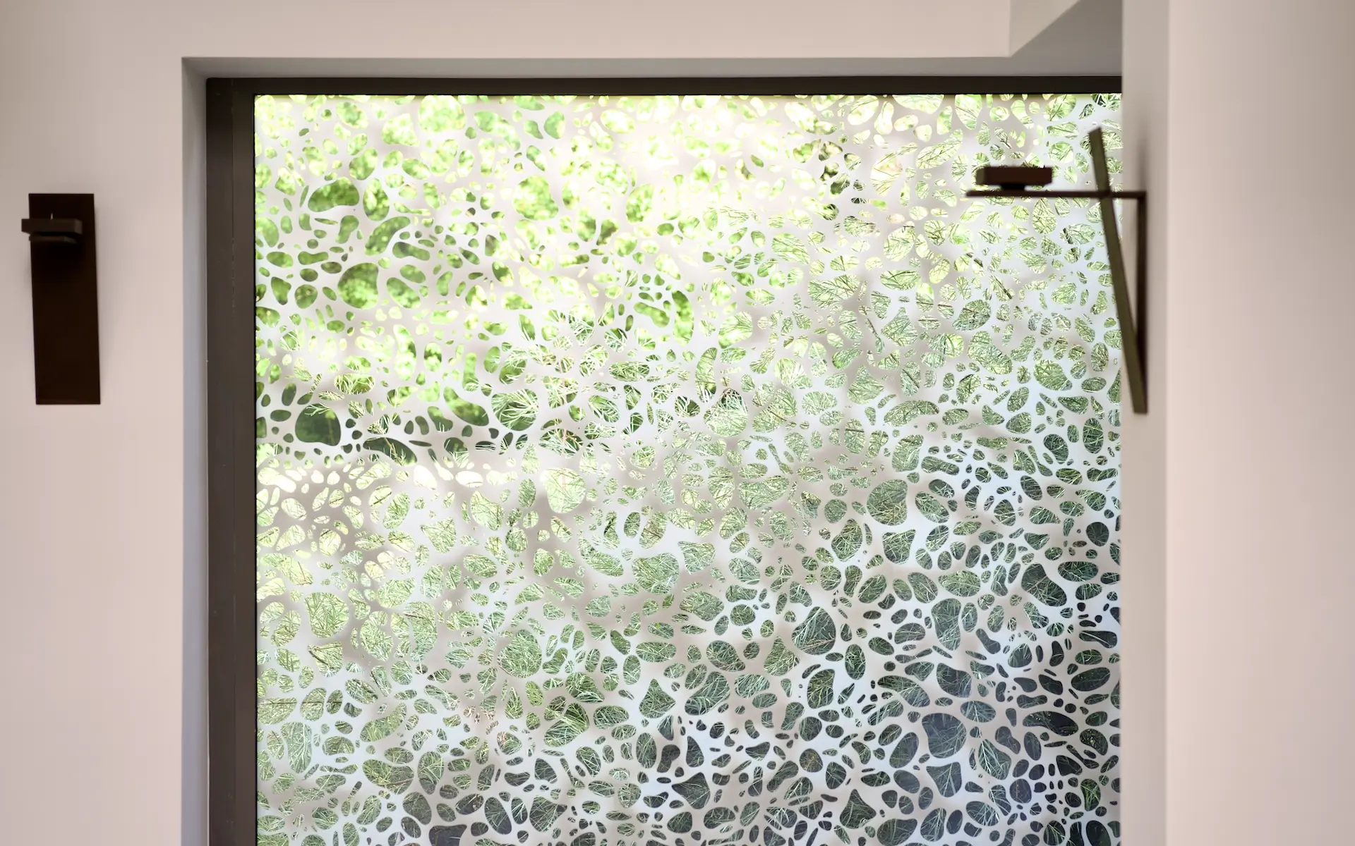 Umbau St. Altfrid in Essen Innenaufnahme vom Eckfenster mit Ornament vor Garten-Ausblick, Apostelleuchtern und Aluminium-Fensterrahmen.