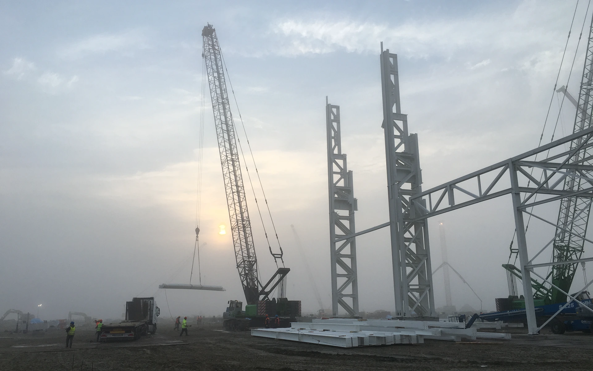 Baustelle Neubau Siemens Windturbinen Fabrik in Cuxhaven mit Baufeld, Errichtung von Fachwerkstützen und Kranarbeiten.