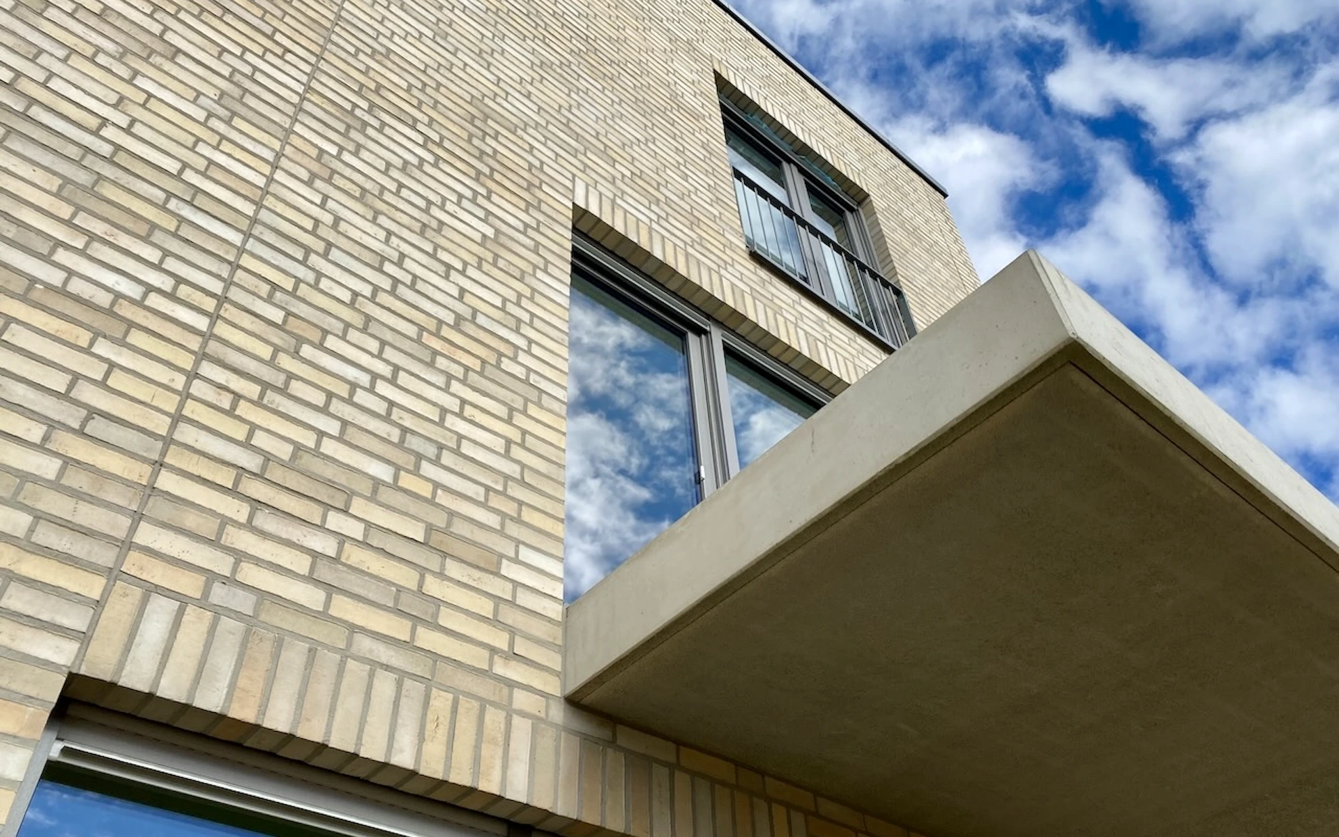 Neubau Mehrfamilienhaus in Ratingen Detail einer Sichtbetonbalkonplatte im Bauzustand mit französischen Fenstern und Klinkerfassade aus Wasserstrichziegeln mit besandeten Dehnfugen.