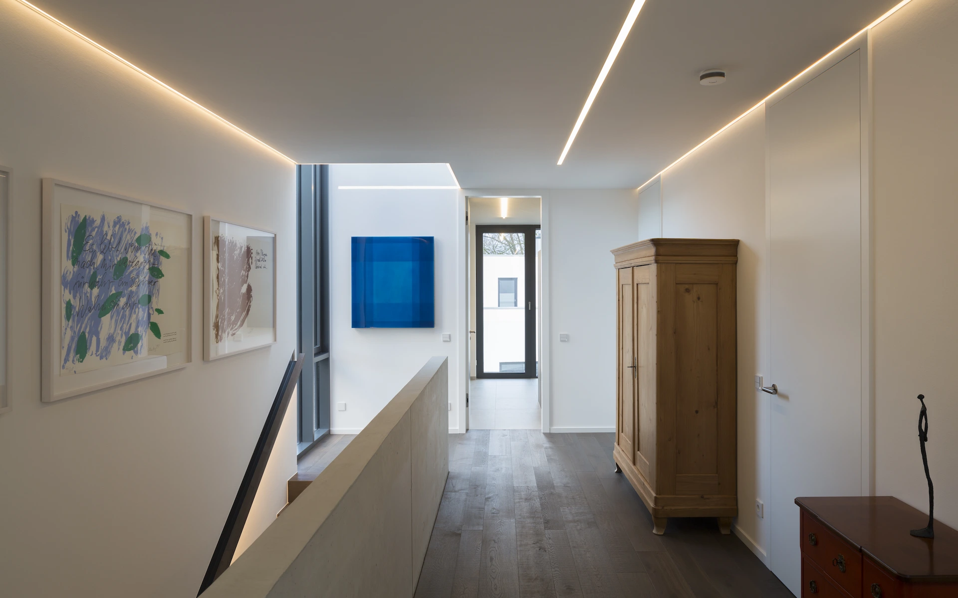 Neubau Haus K in Kamp-Lintfort Flur im Obergeschoss mit in die Dachfläche übergehendem Fenster, großformatigen Parkettdielen, linearen LED-Leuchten und Kunstgegenständen.
