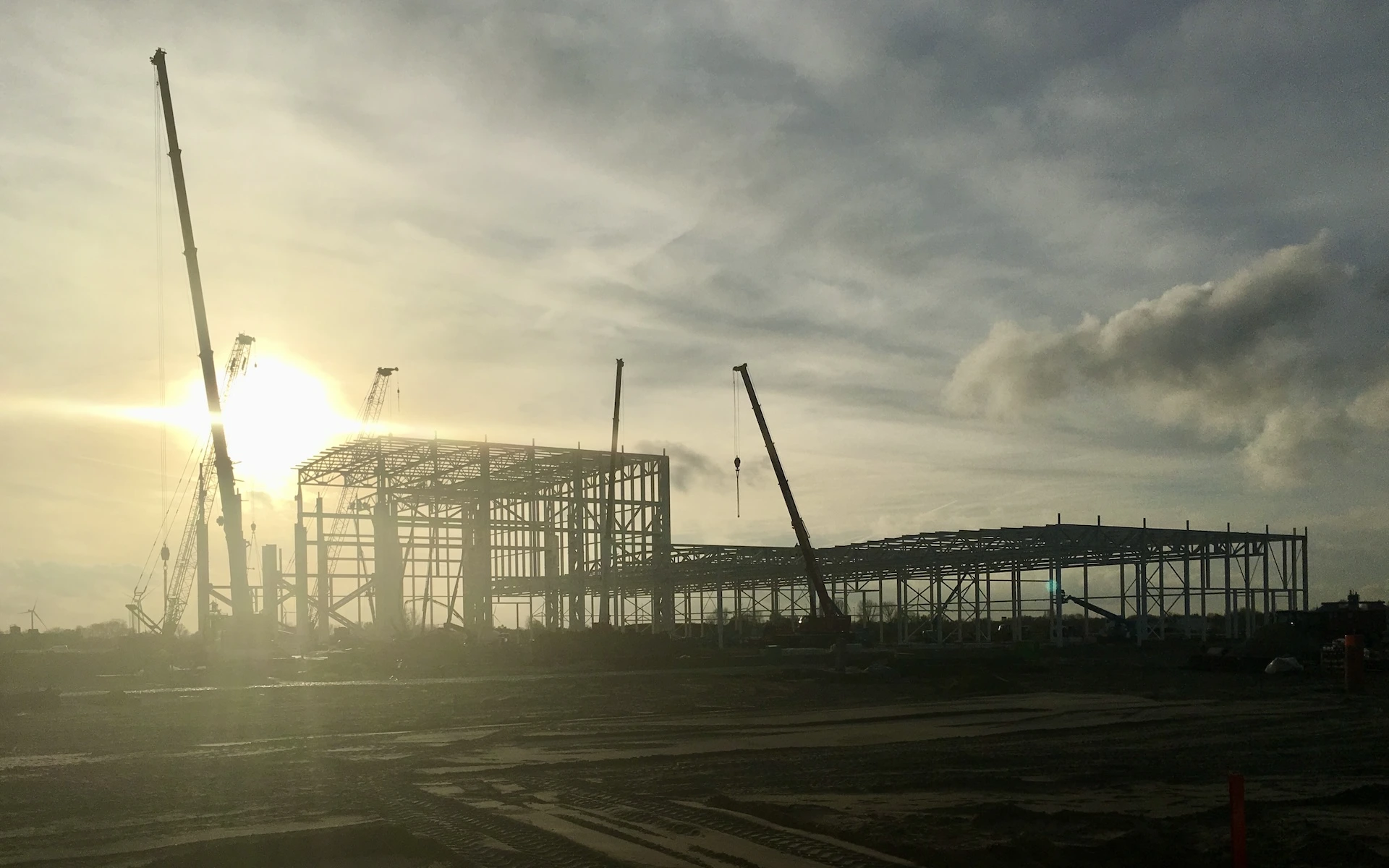 Baustelle Neubau Siemens Windturbinen Fabrik in Cuxhaven mit Baufeld, teilfertiges Stahltragwerk, Baustraßen und Kranarbeiten.