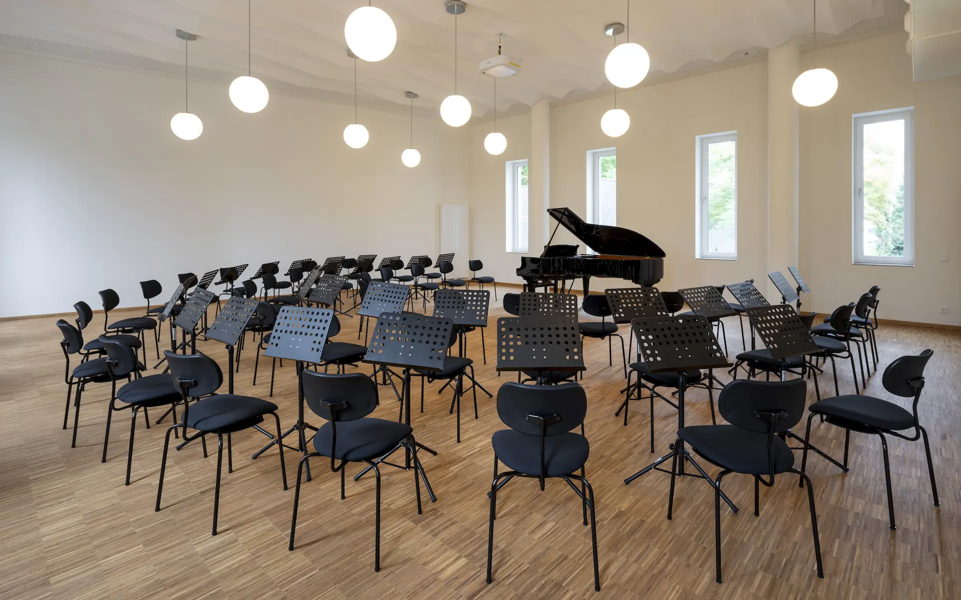 Umbau Haus der Kirchenmusik Essen Innenraum, kleiner Singsaal mit einem zentral angeordneten Flügel, im Kreis gruppierte Stuhlreihen mit Notenständer.